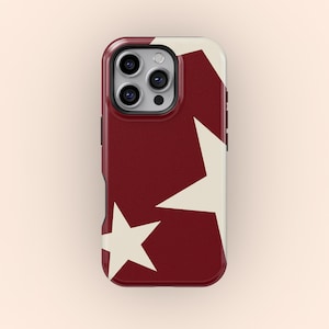 以下が含まれることがあります： クリーム色の星模様が入った、バーガンディ色の携帯電話ケース。ケースは光沢仕上げで、カメラの周りに盛り上がったエッジがあります。デザインは2つの大きな星とテクスチャード加工の背景が特徴です。