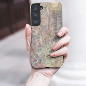 May include: A phone case with a pastel floral and celestial design. The case features a sun, moon, and butterfly motif with the words "radiate love". The case is held in a hand, and the overall aesthetic is soft and whimsical.