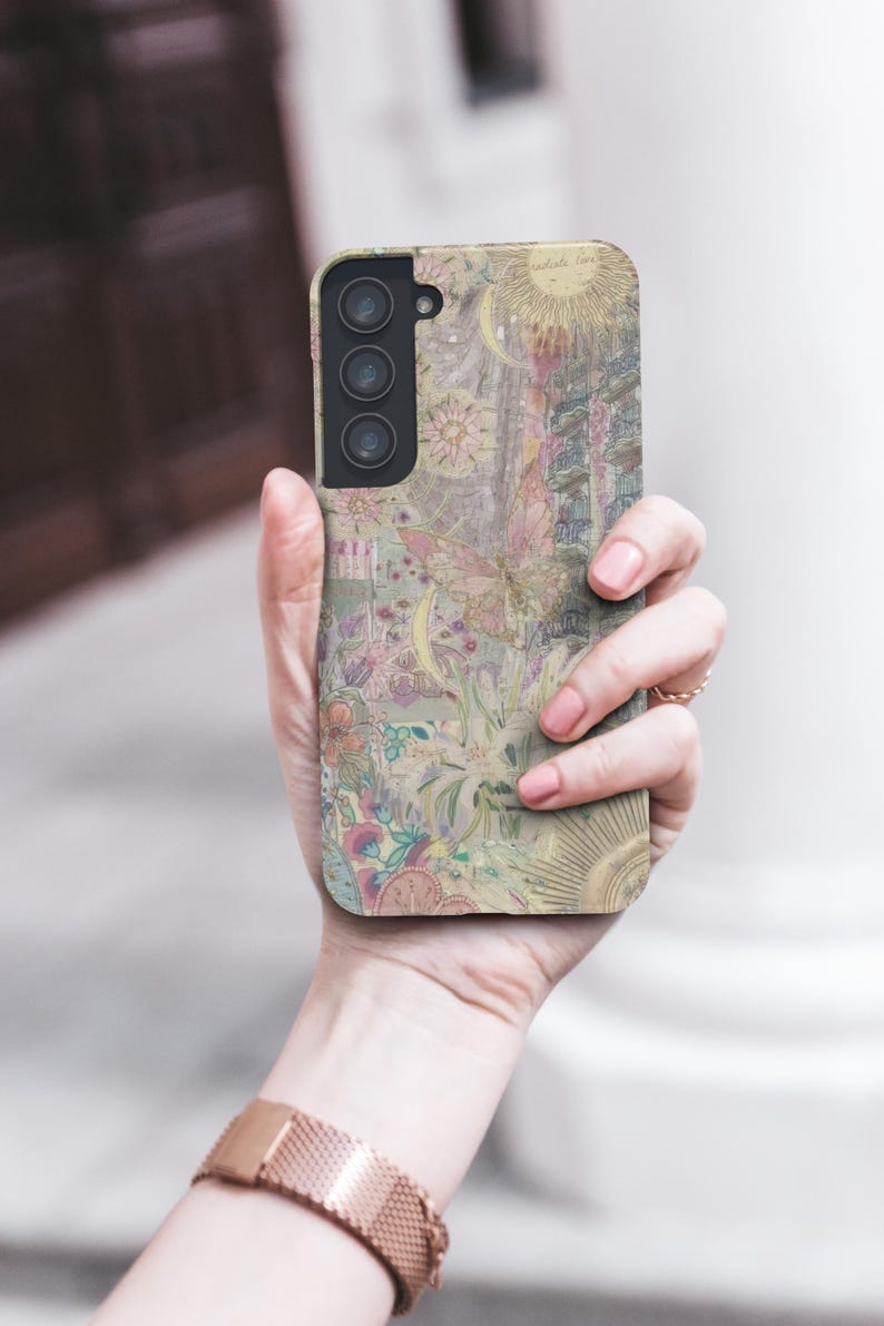May include: A phone case with a pastel floral and celestial design. The case features a sun, moon, and butterfly motif with the words "radiate love". The case is held in a hand, and the overall aesthetic is soft and whimsical.