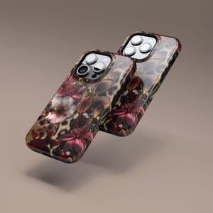 May include: Two phone cases with a floral and leopard print design. The cases feature a glossy finish with a combination of burgundy, brown, and cream colors. The floral pattern includes lilies and other flowers.
