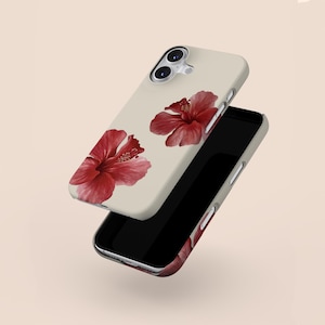 May include: A beige phone case featuring two red hibiscus flowers. The phone case is shown with a black smartphone, showcasing the design. The hibiscus flowers have detailed petals and a vibrant red color.