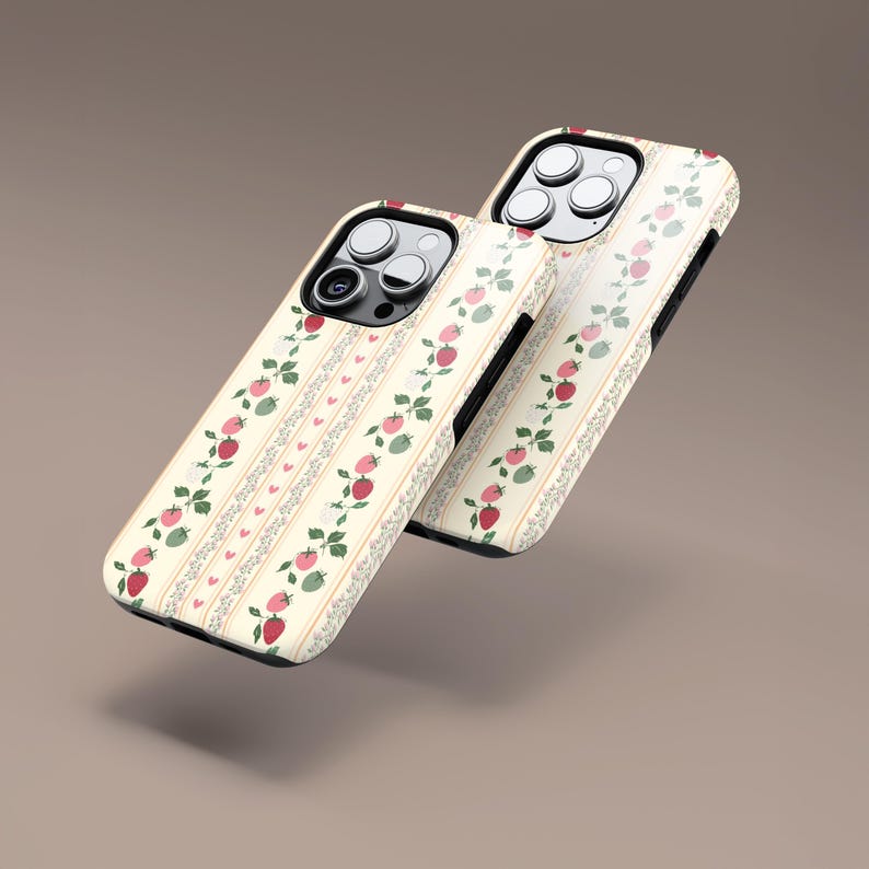 Peut inclure: Deux coques de t&eacute;l&eacute;phone iPhone blanches avec un motif de fraises rouges et vertes et de c&oelig;urs blancs sur un fond cr&egrave;me.