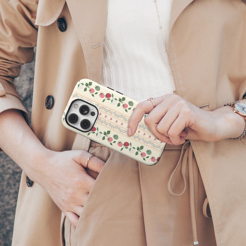 Peut inclure: Une coque de t&eacute;l&eacute;phone iPhone blanche avec un motif floral compos&eacute; de fleurs roses et rouges et de feuilles vertes. La coque a un fond blanc avec un motif d&eacute;licat de lignes grises et de c&oelig;urs.