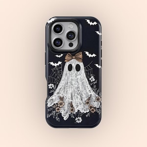 Pode incluir: Capa de telefone preta com um design de fantasma branco, um laço castanho e detalhes florais. O fundo escuro apresenta morcegos brancos e teias de aranha. Um acessório assustador para o Halloween.