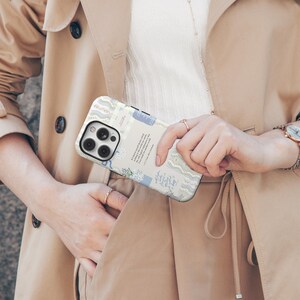 May include: A white iPhone case with a blue and white floral pattern and text. The case has a camera lens cutout and a cutout for the phone's buttons.