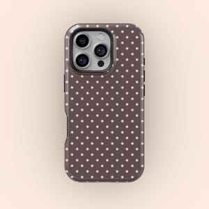 Op de afbeelding: Een telefoonhoesje met een donkerbruine achtergrond en een patroon van kleine, gelijkmatig verdeelde roze stippen. De hoes heeft een glanzende afwerking en een camera-uitsparing.