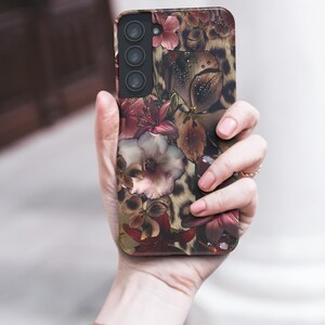 May include: A smartphone case featuring a floral and leopard print design. The case displays a mix of burgundy, pink, and cream-colored flowers against a leopard print background. The case has a camera module with three lenses.