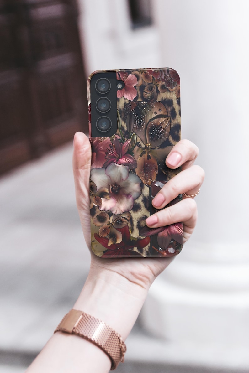 May include: A smartphone case featuring a floral and leopard print design. The case displays a mix of burgundy, pink, and cream-colored flowers against a leopard print background. The case has a camera module with three lenses.