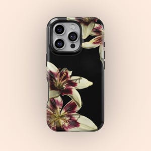 May include: A black phone case with a floral pattern. The design features white petals with burgundy markings, set against a black backdrop. The case has a glossy finish, and the flowers are in a corner.