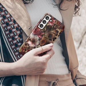 May include: A floral patterned phone case featuring a mix of pink, red, and brown flowers with a leopard print background. The case has a camera cutout with three lenses.