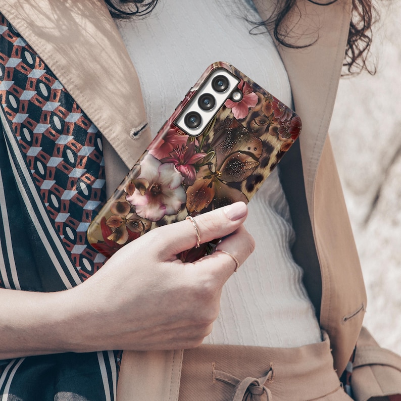 May include: A floral patterned phone case featuring a mix of pink, red, and brown flowers with a leopard print background. The case has a camera cutout with three lenses.
