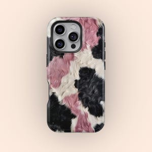 May include: A phone case with a cowhide pattern in black, white, and pink. The case has a glossy finish and a black border. The camera lenses are visible at the top.