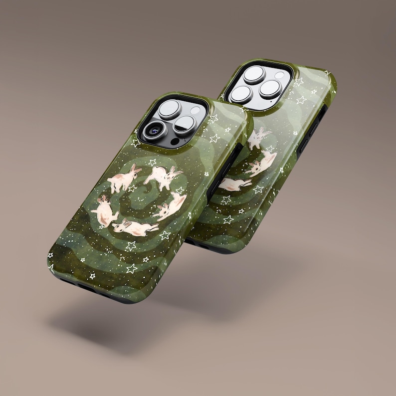 Puede incluir: Dos fundas de tel&eacute;fono verde oliva con un dise&ntilde;o caprichoso. Las fundas presentan un patr&oacute;n de estrellas blancas y una disposici&oacute;n circular de conejos blancos. Las fundas tienen un acabado brillante y un borde verde oscuro.
