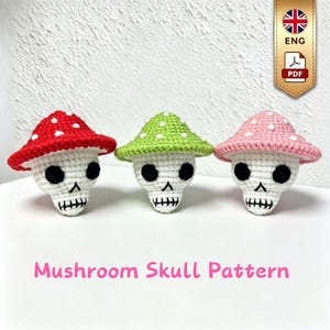 May include: Three crocheted skull figures with mushroom caps in red, green, and pink, each featuring white spots on the cap and black stitched eyes and teeth. The text Mushroom Skull Pattern is displayed in pink at the bottom of the image.