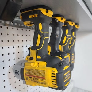 May include: Four yellow and black cordless power drills hang on a pegboard wall. The drills are all the same model and have a black handle with a yellow trigger. The drill on the left has the text "DCF885" and "WARNING: CONSTRUCTION POWER TOOL" printed on the side.