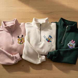 以下が含まれることがあります： ピンク、クリーム、ダークグリーンの3色のクォータージップスウェットシャツ。各スウェットシャツには、プルート、ドナルドダック、デイジーダックの異なる漫画のキャラクターパッチが付いています。スウェットシャツは柔らかい素材で作られています。