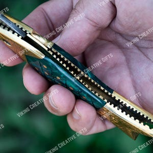 May include: A green and gold pocket knife with a patterned handle. The knife is open and the blade is visible.