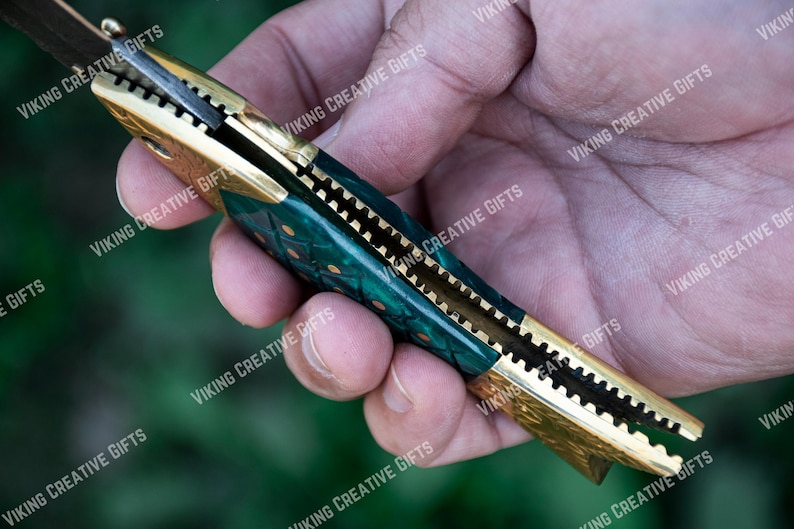 May include: A green and gold pocket knife with a patterned handle. The knife is open and the blade is visible.
