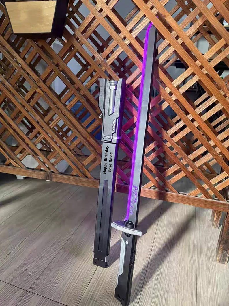 May include: A black and silver sword with a purple blade, resting on a wooden floor. The sword has the text "Happy Birthday Love David" on the sheath and "P.A.R.A.D.O.X" on the blade.