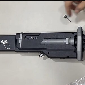 May include: A black and gray sword with the name "THOMAS" in white lettering. The sword has a silver handle and a silver blade. A small silver screw is above the sword.