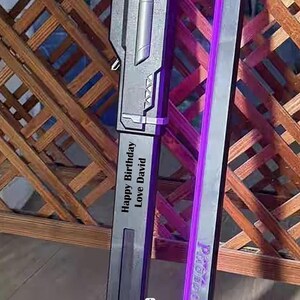 May include: A gray and silver sword with a purple light strip. The sword has the text "Happy Birthday Love David" engraved on the side. The background is a wooden lattice.