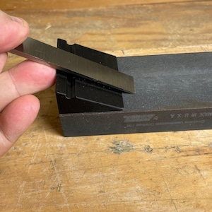 Puede incluir: Una mano sostiene una herramienta de afilado de metal sobre una piedra de afilar negra. La piedra está etiquetada como "King 4000/8000".