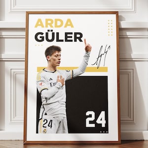 May include: Framed poster featuring Arda Güler in a white and gray soccer uniform. The poster includes the player's name in yellow and black, his signature, and the number 24. The background is white and black.