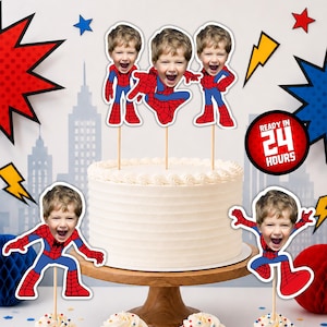 Peut inclure: Un gâteau au glaçage blanc et quatre cupcakes avec des caissettes rouges et bleues, surmontés de décorations personnalisées avec le visage d'un enfant sur un corps de Spider-Man. Les décorations sont sur des bâtonnets. Un badge rouge indique READY IN 24 HOURS.