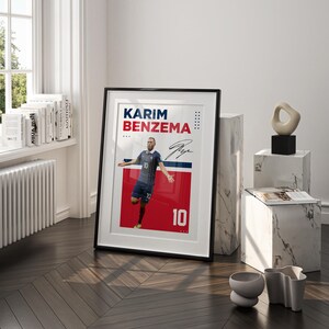 Puede incluir: P&oacute;ster enmarcado con Karim Benzema con uniforme de f&uacute;tbol azul con el n&uacute;mero 10. El p&oacute;ster tiene un fondo rojo y azul con el nombre y la firma del jugador. El marco es negro.