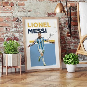 May include: Framed poster featuring Lionel Messi in his Argentina national team uniform. The poster has the text "Lionel Messi" in yellow and navy blue, along with his signature. The image is set against a light blue background.