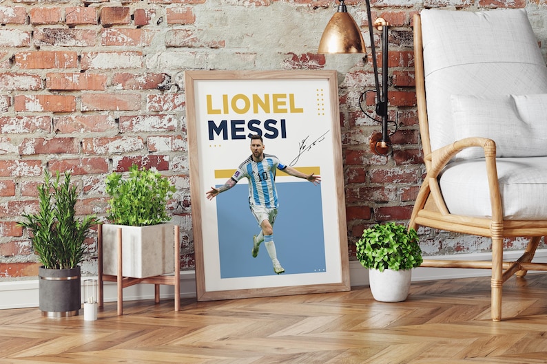 May include: Framed poster featuring Lionel Messi in his Argentina national team uniform. The poster has the text "Lionel Messi" in yellow and navy blue, along with his signature. The image is set against a light blue background.