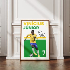 May include: A framed poster featuring soccer player Vin&iacute;cius J&uacute;nior in a yellow and blue uniform, dribbling a soccer ball. The poster includes his name, signature, and the number 7. The background is white and green.