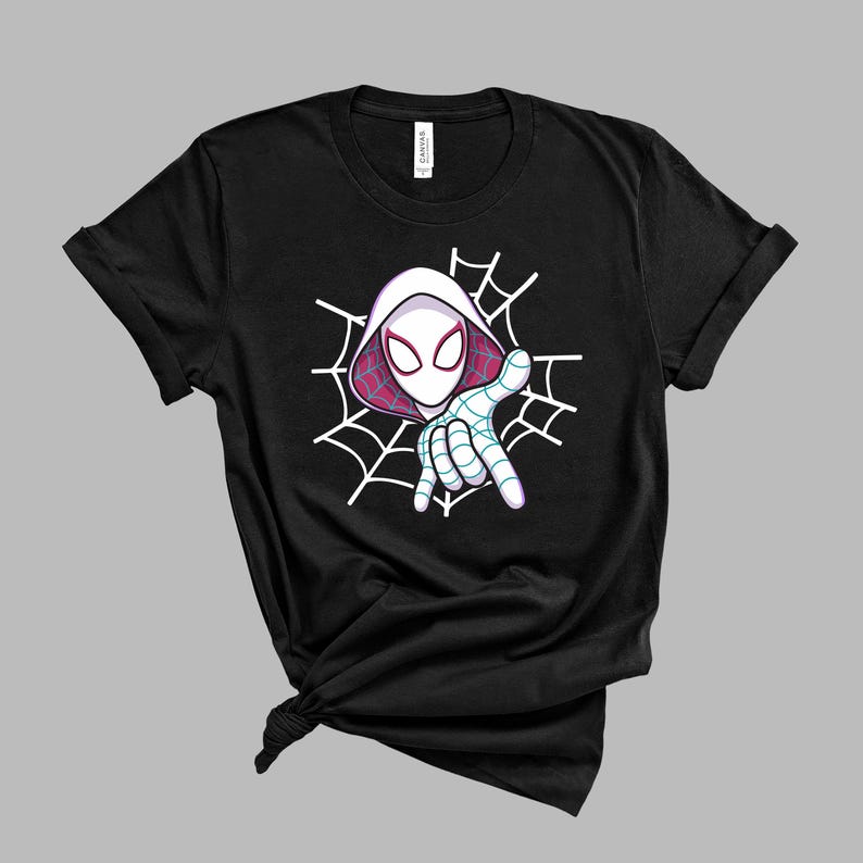 Pu&ograve; includere: Una t-shirt nera a maniche corte con una stampa grafica di un personaggio mascherato con cappuccio bianco e motivi a ragnatela rosa e viola. Il personaggio &egrave; raffigurato dal busto in su con una mano tesa in avanti davanti a una ragnatela.