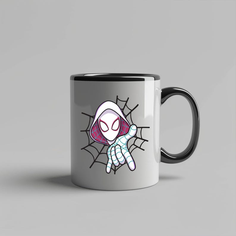 Pu&ograve; includere: Una tazza in ceramica bianca con manico e bordo neri, caratterizzata da una grafica di un personaggio con cappuccio bianco, grandi occhi e una maschera con motivo a ragnatela, su uno sfondo di ragnatela nera con fodera rosa nel cappuccio.
