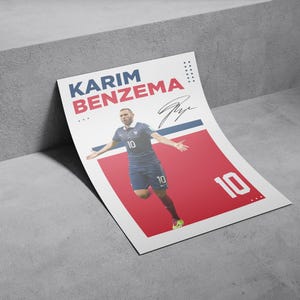 Puede incluir: Un p&oacute;ster de Karim Benzema con uniforme de f&uacute;tbol azul con el n&uacute;mero 10. El p&oacute;ster tiene un fondo rojo y blanco con el nombre y la firma del jugador. El p&oacute;ster est&aacute; apoyado contra una superficie gris.