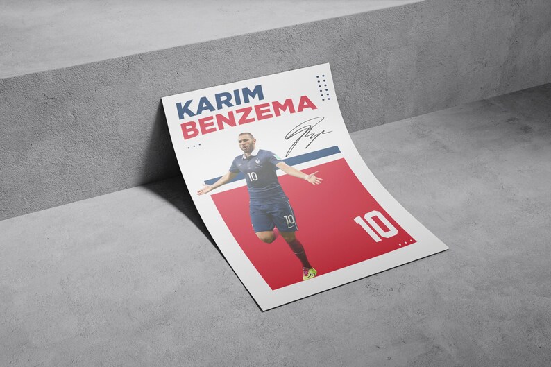 Puede incluir: Un p&oacute;ster de Karim Benzema con uniforme de f&uacute;tbol azul con el n&uacute;mero 10. El p&oacute;ster tiene un fondo rojo y blanco con el nombre y la firma del jugador. El p&oacute;ster est&aacute; apoyado contra una superficie gris.