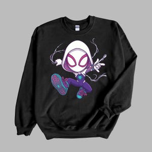 May include: A black crewneck sweatshirt featuring a graphic illustration of a stylized character wearing a white hood, a purple and white suit with a spider emblem, and teal sneakers with pink laces, depicted in a dynamic jumping pose.