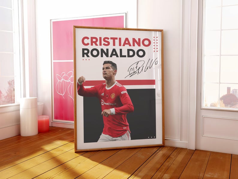 May include: A framed poster featuring Cristiano Ronaldo in a red soccer jersey. The poster has the name "CRISTIANO RONALDO" in large red and black letters, along with his signature. The image is set against a white and black background.
