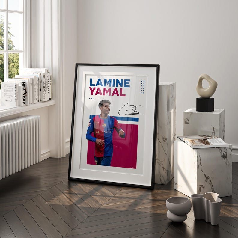 May include: Framed poster featuring Lamine Yamal in a Barcelona jersey, with his name in blue and red text. The poster includes an autograph and is displayed on a wooden floor, leaning against a white marble block.