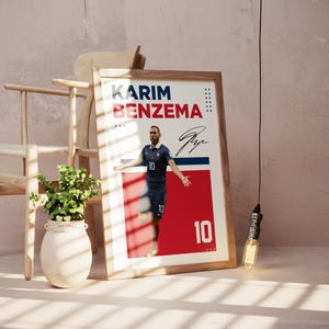 Puede incluir: P&oacute;ster enmarcado con Karim Benzema con uniforme de f&uacute;tbol azul, n&uacute;mero 10. El p&oacute;ster tiene un dise&ntilde;o rojo y blanco con el nombre y la firma del jugador. Una silla de madera y una planta en un jarr&oacute;n blanco est&aacute;n en el fondo.