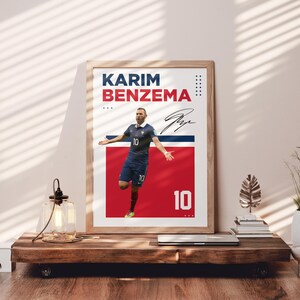 Puede incluir: P&oacute;ster enmarcado de Karim Benzema con uniforme azul, n&uacute;mero 10. El p&oacute;ster tiene un fondo rojo y azul con el nombre y la firma del jugador. El p&oacute;ster se exhibe sobre una mesa de madera, con otros objetos decorativos.