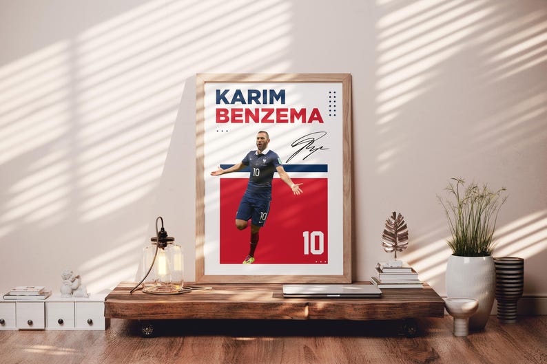 Puede incluir: P&oacute;ster enmarcado de Karim Benzema con uniforme azul, n&uacute;mero 10. El p&oacute;ster tiene un fondo rojo y azul con el nombre y la firma del jugador. El p&oacute;ster se exhibe sobre una mesa de madera, con otros objetos decorativos.