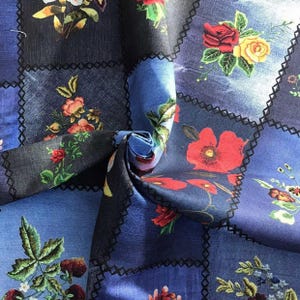 Peut inclure: Un tissu floral bleu avec un motif patchwork. Le tissu présente des carrés de différentes nuances de bleu et de gris foncé, chacun orné de motifs floraux colorés, notamment des roses et des coquelicots. Les bords des carrés sont soulignés de coutures noires.