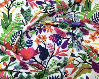 May include: White fabric with a vibrant floral pattern. The design features a variety of colorful flowers and leaves in shades of pink, orange, purple, green, and blue. The fabric is folded, showing the detailed print.