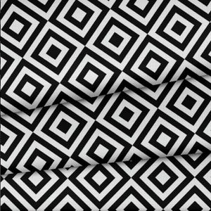May include: Black and white geometric fabric with a repeating pattern of squares within squares. The fabric is folded, creating shadows and texture. The design is a bold, graphic statement.