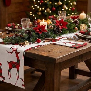 Könnte beinhalten: Ein weißer Tischläufer und eine passende Serviette mit einem rot-grünen Karomuster aus Rentieren. Das Textil misst 140 mal 45 cm. Der Läufer liegt auf einem Holztisch mit einem Mittelstück aus Tannenzweigen, roten Weihnachtssternen, Tannenzapfen und Kerzen.