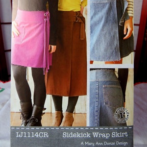 Könnte beinhalten: Ein Schnittmuster für einen Wickelrock, genannt "Sidekick Wrap Skirt", entworfen von Mary Ann Donze. Das Schnittmuster stammt aus der Crossroads-Linie von Amy Barickman. Das Schnittmuster zeigt einen Jeansrock, einen braunen Rock und einen rosa Rock.