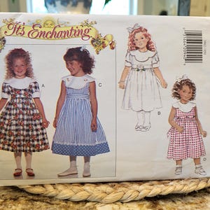 May include: A sewing pattern for girls' dresses. The pattern includes four different styles: a plaid dress with a white collar, a striped dress with a white collar, a white dress with a white collar, and a gingham dress with a white collar. The pattern is from Butterick and is size 5-6X.