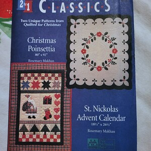 Puede incluir: Una portada de libro con dos patrones de acolchado para Navidad. El primer patrón es un acolchado de poinsettia, de 80 pulgadas por 92 pulgadas. El segundo patrón es un acolchado de calendario de Adviento de San Nicolás, de 18 1/2 pulgadas por 26 1/2 pulgadas. Ambos patrones son de Rosemary Makhan.