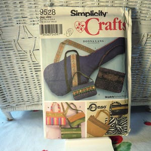 May include: A Simplicity Crafts sewing pattern envelope, number 9528, featuring illustrations of various handmade bags including a guitar case, shoulder bags, and totes with diverse fabric textures, patterns, and decorative trim details.